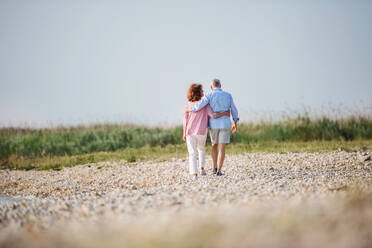 Rückansicht eines älteren Paares im Urlaub bei einem Spaziergang am See, das Arm in Arm geht. - HPIF27026