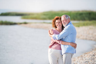 Front view of senior couple on a holiday on a walk by the lake, hugging. - HPIF27030