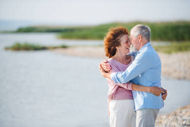 A senior couple on a holiday on a walk by the lake, hugging. Copy space. - HPIF27031