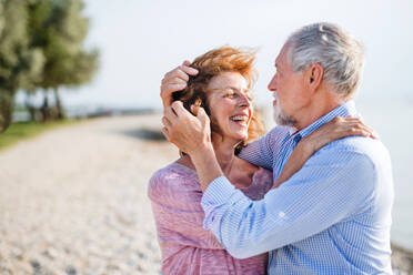 Front view of senior couple on a holiday on a walk by the lake, hugging. - HPIF27036