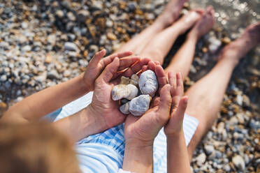 Draufsicht auf den Vater und die kleine Tochter im Urlaub, die am See sitzen und Steine in der Hand halten, Mittelteil. - HPIF27045