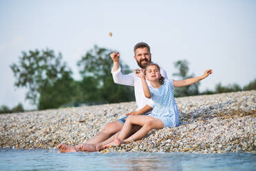 Father and small daughter on a holiday sitting by the lake or sea. - HPIF27047