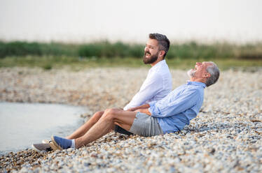 Älterer Vater und erwachsener Sohn sitzen lachend am See und kopieren den Raum. - HPIF27064