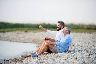 Älterer Vater und erwachsener Sohn sitzen am See und unterhalten sich. Kopierraum. - HPIF27065