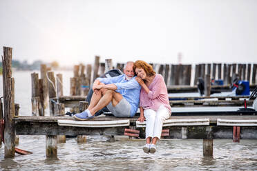 Verliebtes älteres Paar im Urlaub am See sitzend, sich umarmend. - HPIF27074