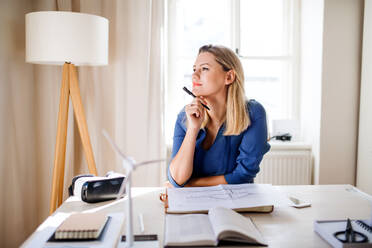 Junge Frau Architektin sitzt am Schreibtisch drinnen im Büro zu Hause, arbeiten. - HPIF27090