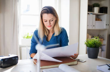 Young woman architect sitting at the desk indoors in home office, working. - HPIF27091