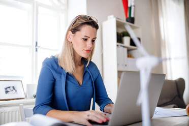 Junge Frau Architektin mit Laptop sitzt am Schreibtisch drinnen im Büro zu Hause, arbeiten. - HPIF27097