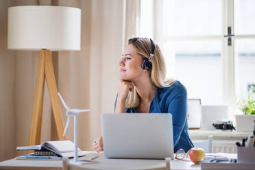 A young woman engineer with headphones sitting at the desk indoors in home office. - HPIF27099