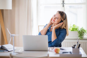 Young woman with laptop and headphones sitting at the desk indoors in home office. - HPIF27100