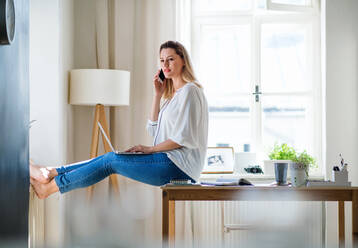Eine junge Frau mit Smartphone und Laptop in einem Büro zu Hause bei der Arbeit. - HPIF27103