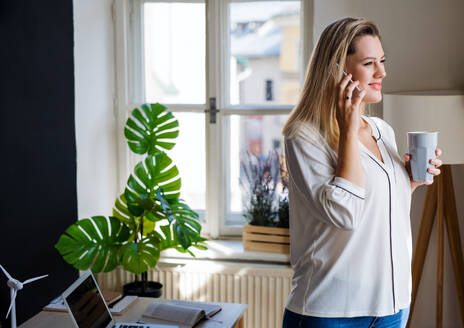 Junge Frau mit Smartphone, die in einem Haus im Büro steht und während der Arbeit telefoniert. - HPIF27104