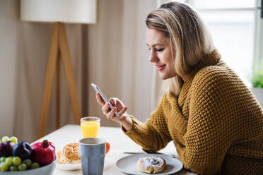 Junge Frau, die zu Hause am Tisch sitzt und beim Entspannen ihr Smartphone benutzt. - HPIF27115