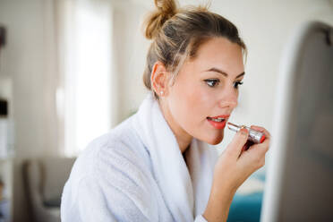A young woman indoors at home in the morning, putting on lipstick. - HPIF27120