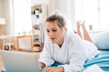 Eine junge Frau, die morgens zu Hause auf dem Bett liegt und einen Laptop benutzt. - HPIF27132