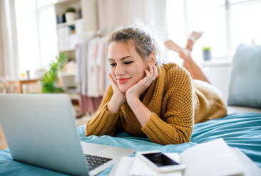 Happy young woman with laptop lying on bed indoors at home, relaxing. - HPIF27134