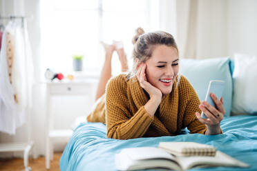 Happy young woman with smartphone lying on bed indoors at home, relaxing. - HPIF27136