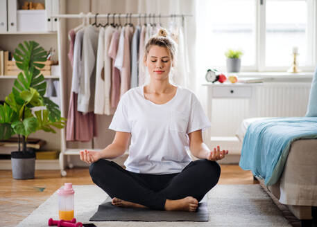Vorderansicht einer jungen Frau, die zu Hause Yogaübungen macht und meditiert. - HPIF27137