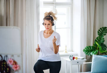A young woman with headphones doing exercise in bedroom indoors at home. - HPIF27143