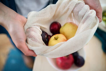 Mittelteil einer Frau, die Obst in einer wiederverwendbaren Tasche zu Hause aufbewahrt, Konzept des nachhaltigen Lebensstils. - HPIF27152