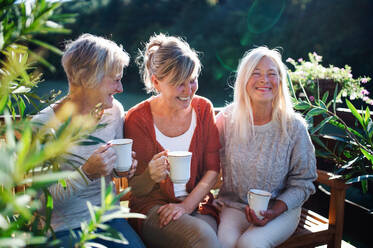Group of senior women friends with coffee sitting outdoors on terrace, resting. - HPIF27164