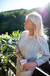 Seitenansicht einer älteren Frau mit Kaffee, die auf einer Terrasse steht und sich ausruht. - HPIF27167