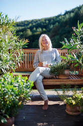 Vorderansicht einer älteren Frau mit Kaffee, die auf der Terrasse sitzt und sich ausruht. - HPIF27170