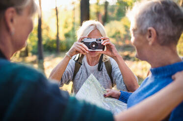 Happy senior women friends walking outdoors in forest, taking photos with camera. - HPIF27198