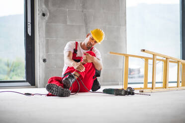 An accident of a male worker at the construction site. A man with an injured leg sitting on the floor. - HPIF27221