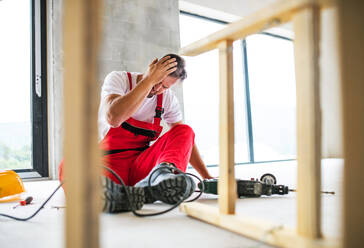 An accident of a male worker at the construction site. A man with an injured head sitting on the floor. - HPIF27223