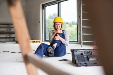 Accident of a female worker at the construction site. A woman in pain with an injured leg sitting on the floor. - HPIF27229