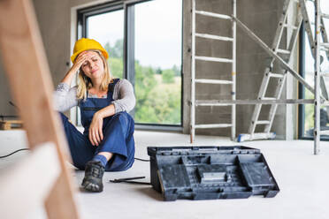 Accident of a female worker at the construction site. A woman with an injured head sitting on the floor. - HPIF27230