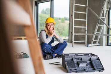 Portrait of a female worker on the construction site. Beautiful young woman sitting on the floor. - HPIF27233