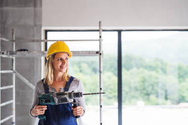 Portrait of a female worker on the construction site. Beautiful young woman holding an electric drill. Copy space. - HPIF27234