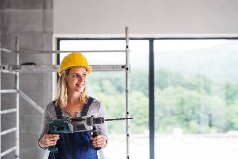 Porträt einer Arbeiterin auf der Baustelle. Schöne junge Frau hält eine elektrische Bohrmaschine. Raum kopieren. - HPIF27234