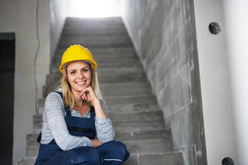 Junge Arbeiterin mit gelbem Helm auf der Treppe einer Baustelle sitzend, Raum kopieren. - HPIF27237