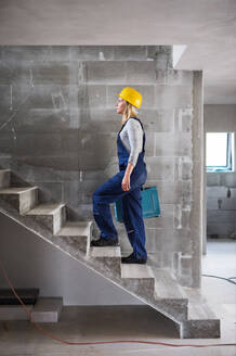 Junge Arbeiterin mit einem Werkzeugkasten, die auf der Baustelle die Treppe hinaufgeht. Raum kopieren. - HPIF27243