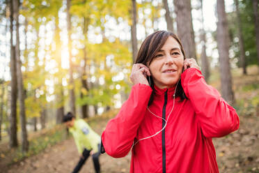 Two active female runners stretching outdoors in forest in autumn nature after the run. - HPIF27267