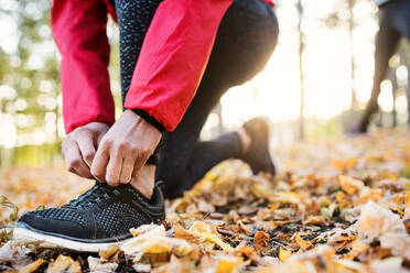 A midsection view of hands of female runner outdoors in autumn nature, tying shoelaces. - HPIF27274