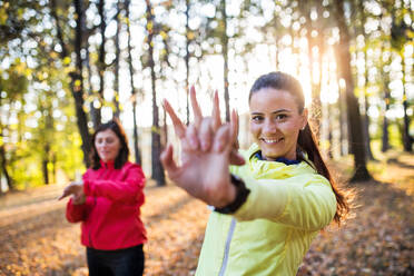 Zwei aktive Läuferinnen dehnen sich nach ihrem Lauf im Wald in der herbstlichen Natur. - HPIF27281