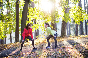 Two active female runners stretching outdoors in forest in autumn nature after he run. - HPIF27289