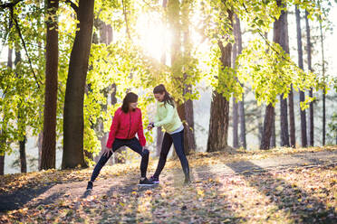 Zwei Läuferinnen mit Smartwatch stehen auf einer Straße im Wald in herbstlicher Natur und messen oder überprüfen die Zeit. - HPIF27290