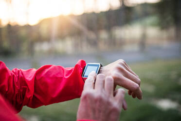 Eine Mittelansicht der Hände einer Läuferin mit Smartwatch im Freien in herbstlicher Natur, die die Zeit überprüft. - HPIF27301