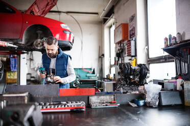 Älterer Mann, der ein Auto in einer Garage repariert. - HPIF27315