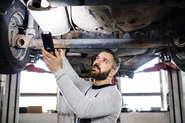 Mature man mechanic repairing a car in a garage. - HPIF27320