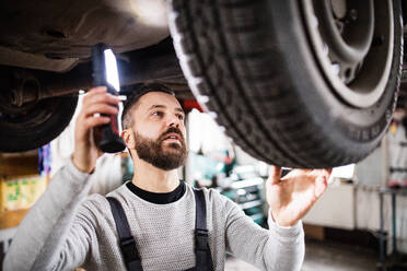 Älterer Mann, der ein Auto in einer Garage repariert. - HPIF27323