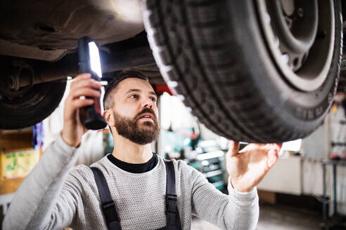 Älterer Mann, der ein Auto in einer Garage repariert. - HPIF27323