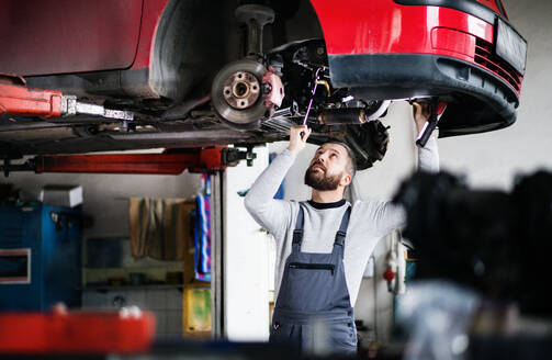 Älterer Mann, der ein Auto in einer Garage repariert. - HPIF27325