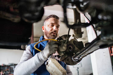 Mature man mechanic repairing a car in a garage. - HPIF27330