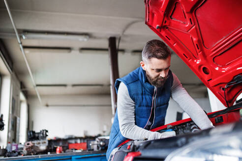 Älterer Mann, der ein Auto in einer Garage repariert. - HPIF27334